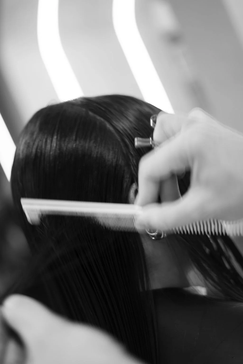 Detalhe do corte: pente e mão separando uma mecha de cabelo escuro